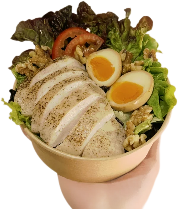 Hand holding a Power Salad bowl with sliced chicken breast, marinated eggs, walnuts and leafy greens
